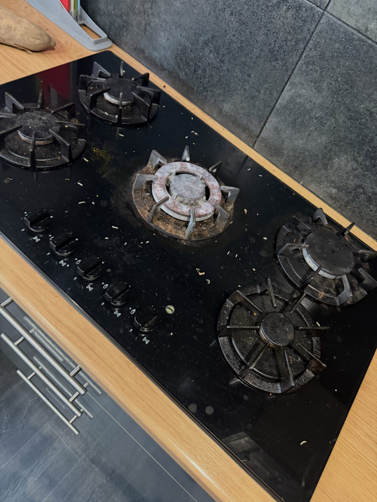 A greasy gas hob before cleaning on a communal job